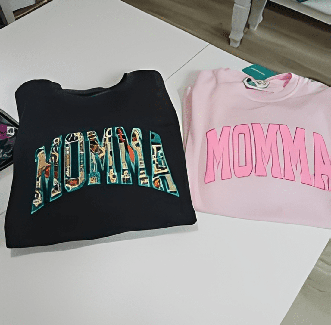 Black and pink "Momma" sweatshirts on table.